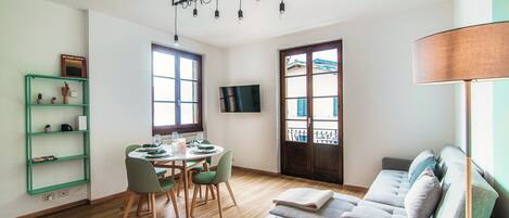 Una sala moderna con sofá, una mesa de comedor con sillas, un televisor montado en la pared y un ventanal con vistas al exterior.
