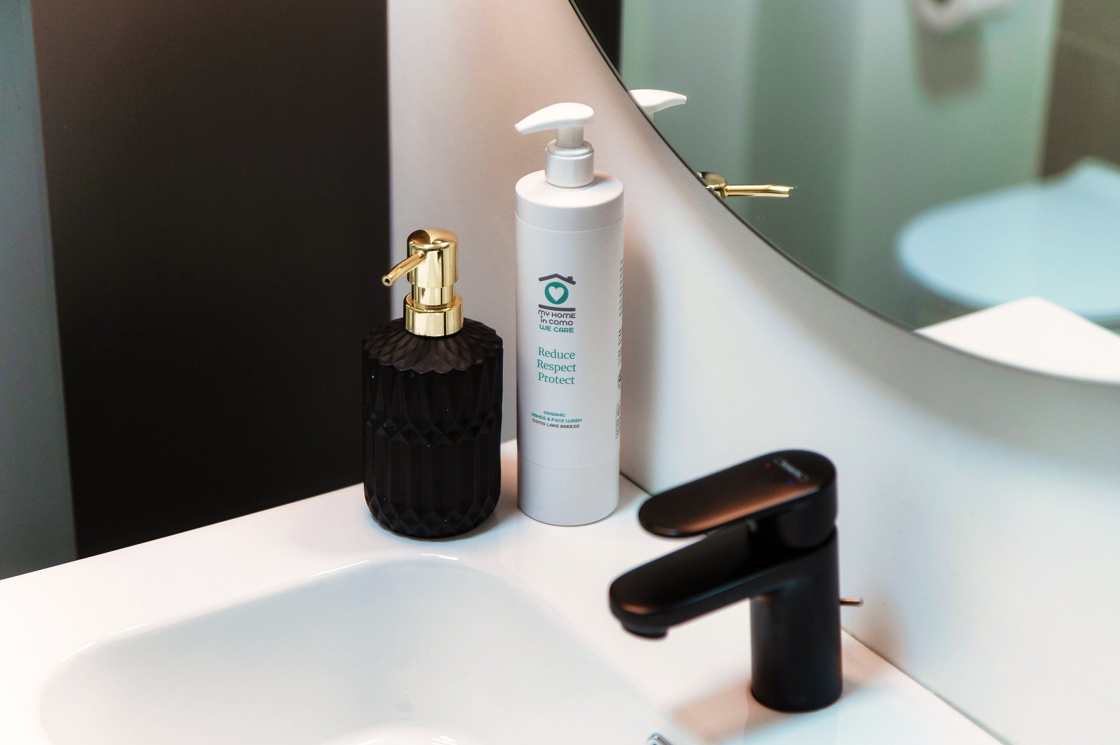 A bathroom sink with a gold faucet, a black soap dispenser, and a white bottle of hand soap.