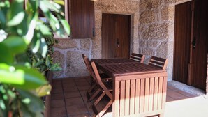 An outdoor patio with a wooden table and chairs, stone walls, and wooden doors. - Aldeia da Quinta do Paço- Casa do Curral (São Salvador do Campo)