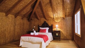A cozy bedroom with a wooden ceiling, a large bed with white bedding and a red pillow, a bedside table with a lamp, and a window on the right. - Aldeia da Quinta do Paço- Casa do Curral (São Salvador do Campo)