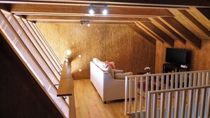 A loft-style room with a sloped ceiling, wooden beams, a white sofa, a television, and a small table with a flower vase. - Aldeia da Quinta do Paço- Casa do Curral (São Salvador do Campo)