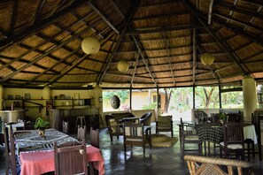 A spacious dining area with a thatched roof, wooden furniture, and a view of the outdoors. - Mango Tree Lodge (Thakudwara)