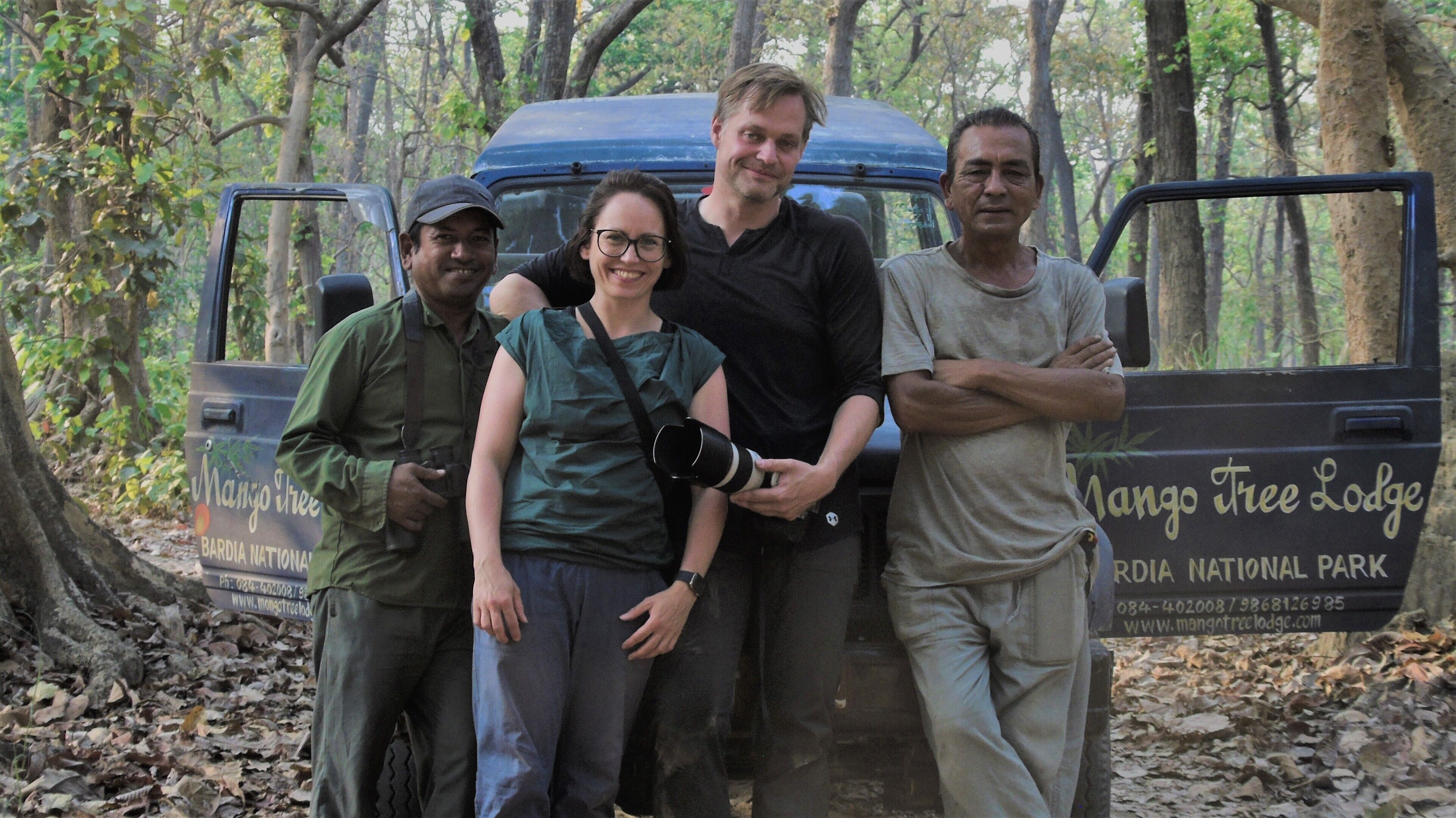 Un groupe de personnes se tient devant un véhicule sur lequel on peut lire les inscriptions « Mangotree Lodge » et « Parc national de Bardia ».