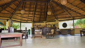 A spacious, open-air room with a thatched roof, wooden furniture, and a bar area. - Mango Tree Lodge (Thakudwara)