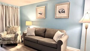 A living room with a sofa, a patterned armchair, a lamp, and two framed pictures on the wall. - Amazing Oceanfront 1 Bedroom (Myrtle Beach)