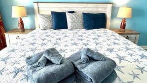 A bed with a star-patterned bedspread, two pillows, two bedside lamps, and a framed sign on the wall. - Amazing Oceanfront 1 Bedroom (Myrtle Beach)