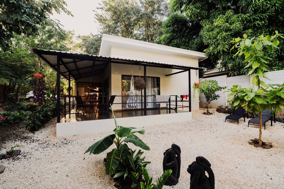 Una casa moderna con un porche cubierto, un comedor y un jardín con diversas plantas.