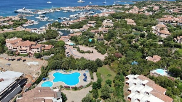 Ett flygbildsfoto av en kuststad med en småbåtshamn, bostadshus och ett område med en swimmingpool.