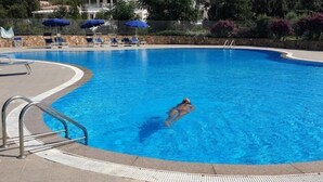 En swimmingpool med en person som simmar, solstolar och parasoller.