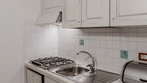 Ett kök med vita skåp, en diskho i rostfritt stål, en gasspis och en brödrost.