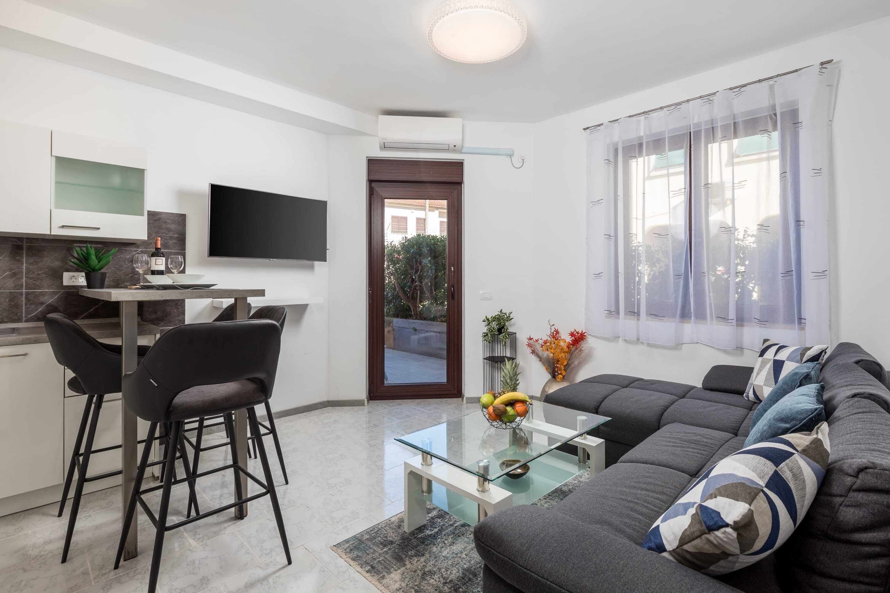 Apartamento moderno com cozinha, sala de jantar e sala de estar. Possui televisão de tela plana, sofá e mesa de centro.