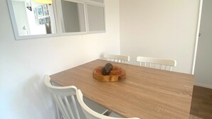 Un coin repas avec une table en bois, des chaises blanches, un luminaire suspendu et un miroir au mur.