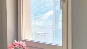 A room with a window overlooking a cityscape, a small table with a potted orchid, and a chair. - Alimos Sea View Family Apartment (Alimos)