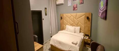 A hotel room with a large bed, a desk, a chair, and a small table.