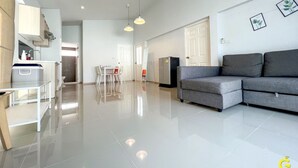 A spacious living area with a grey sofa, a small table, and a white cabinet. There is a door leading to another room and a refrigerator in the corner. - GAO Akira Pool Villa (Ban Chang)