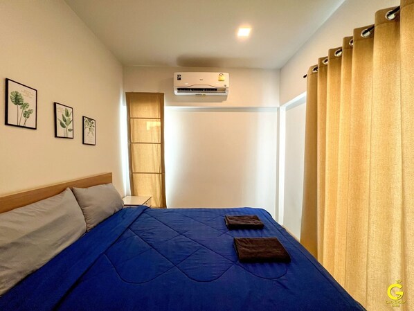 Habitación de hotel con cama, aire acondicionado, cortinas e impresiones botánicas enmarcadas en la pared.