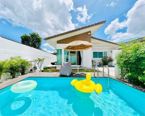 Una piscina con flotadores, una silla y una sombrilla de paja.