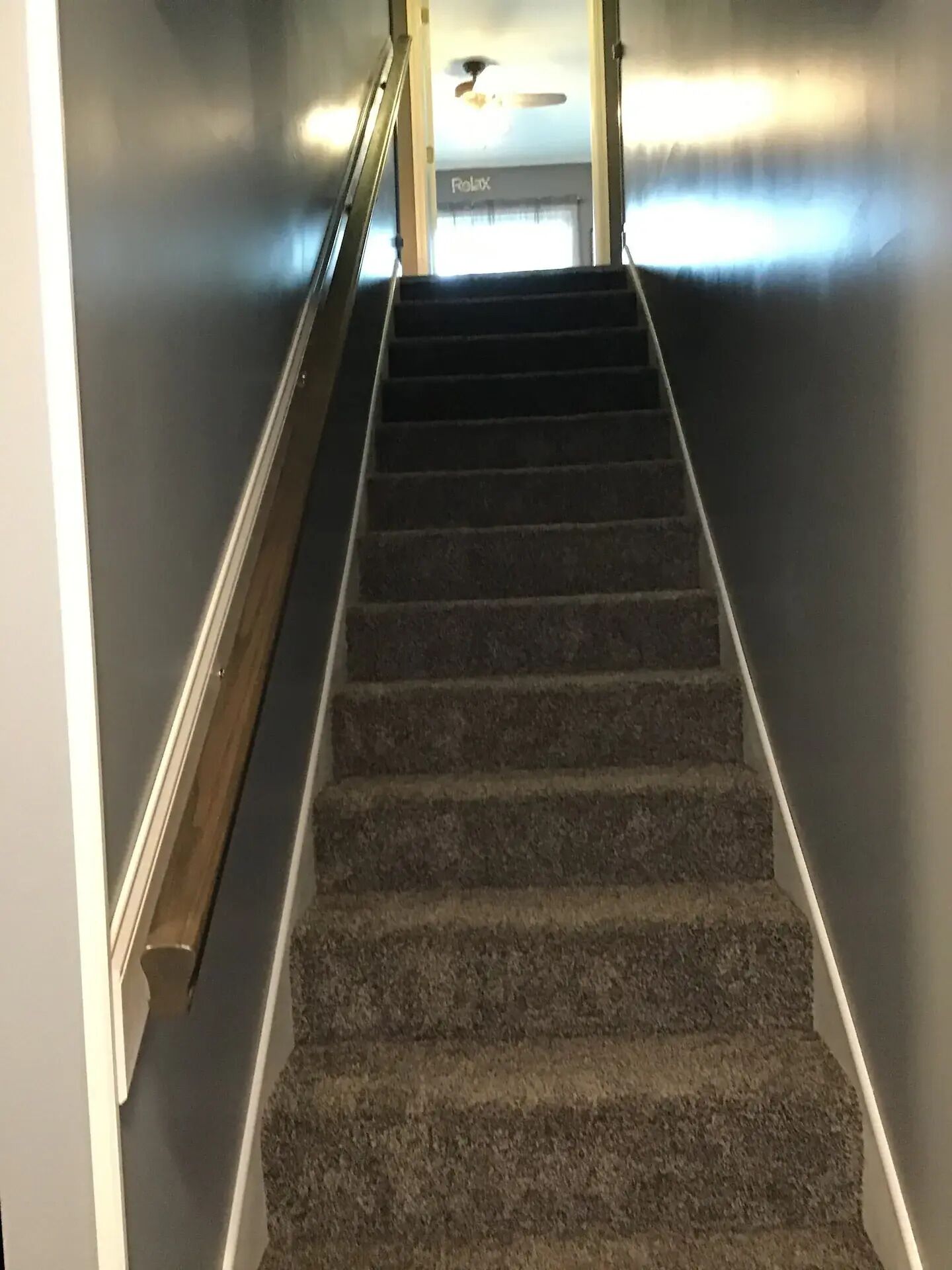 A carpeted staircase with a handrail, leading to a room with a ceiling fan and a sign that reads "Relax".