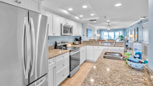 A modern kitchen with white cabinetry, stainless steel appliances, granite countertops, and a central island with a sink. - Intracoastal and Gulf of Mexico water views from this hideaway unit complete with heated pool, hot tub & home office (Indian Shores)