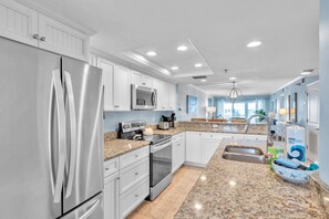 A modern kitchen with white cabinetry, stainless steel appliances, granite countertops, and a central island with a sink. - Intracoastal and Gulf of Mexico water views from this hideaway unit complete with heated pool, hot tub & home office (Indian Shores)