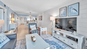A spacious living room with a large TV, a dining area, and a kitchen in the background. - Intracoastal and Gulf of Mexico water views from this hideaway unit complete with heated pool, hot tub & home office (Indian Shores)