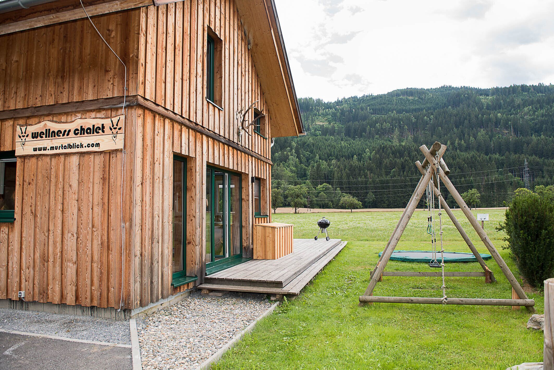 A wooden building with a sign for 'wellness chalet' and a wooden swing set in a grassy area.