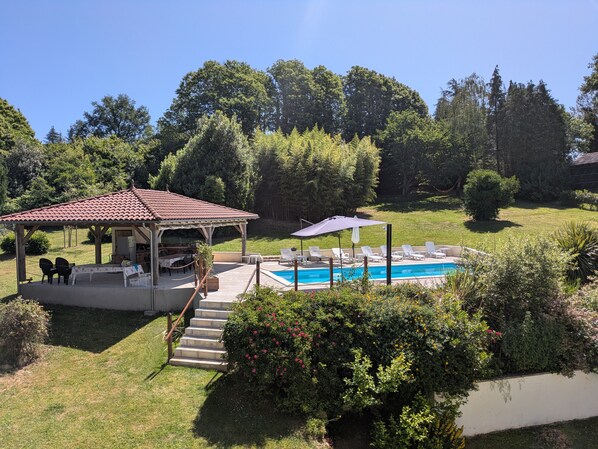 A covered outdoor seating area with a pool, surrounded by greenery and trees.