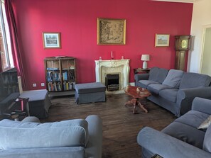 Uma sala de estar com lareira, sofá, estante de livros e relógio.