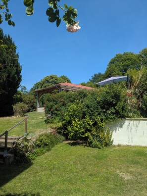 A garden with a pergola, a white wall, and a red-tiled roof structure.