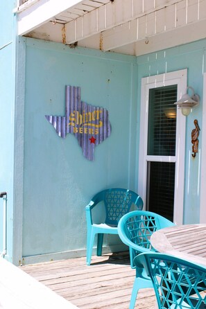 A blue exterior wall with a Texas state outline and 'Shiner Beers' sign, a wooden deck, and a table with chairs. - Bayfront bayside condo (Rockport)