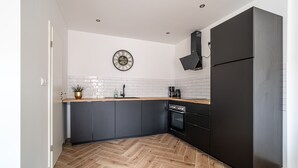 A modern kitchen with dark cabinetry, a herringbone wood floor, a round clock on the wall, and a black refrigerator.