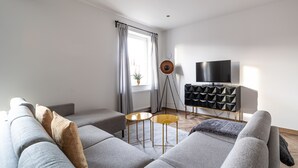 A modern living room with a grey sofa, a small yellow table, and a black entertainment unit with a TV.