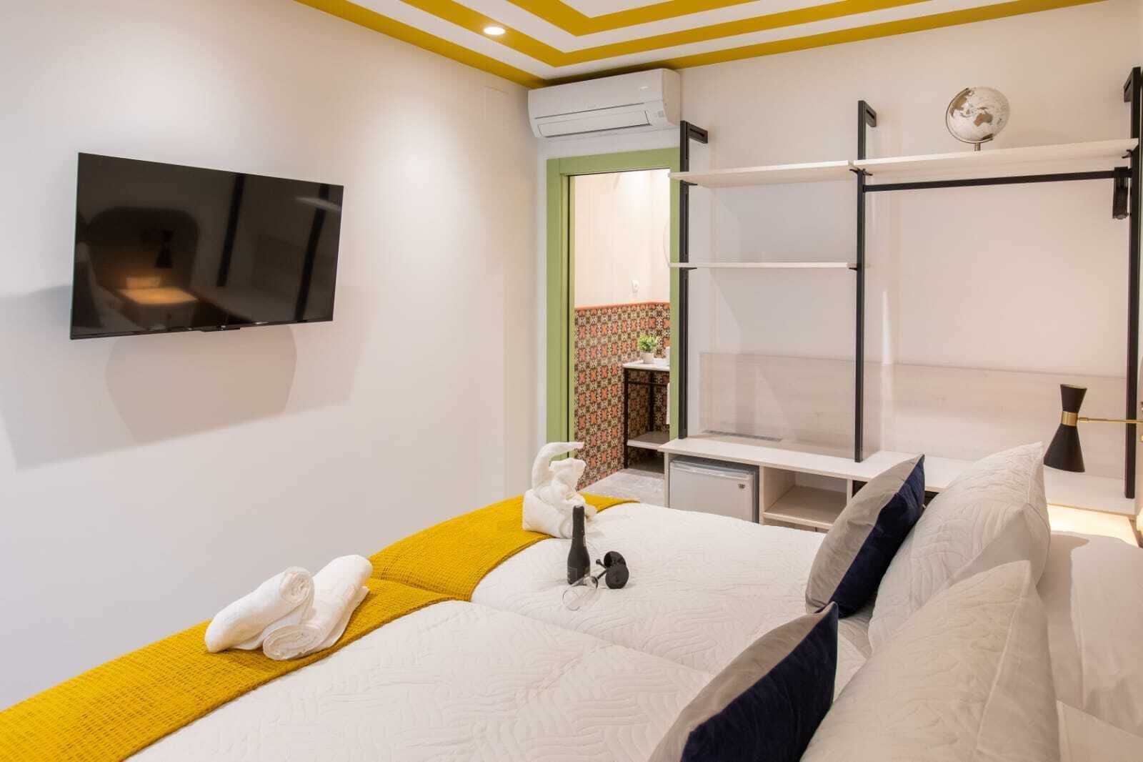 A hotel room with a bed, a TV mounted on the wall, a small desk, and a mirror.