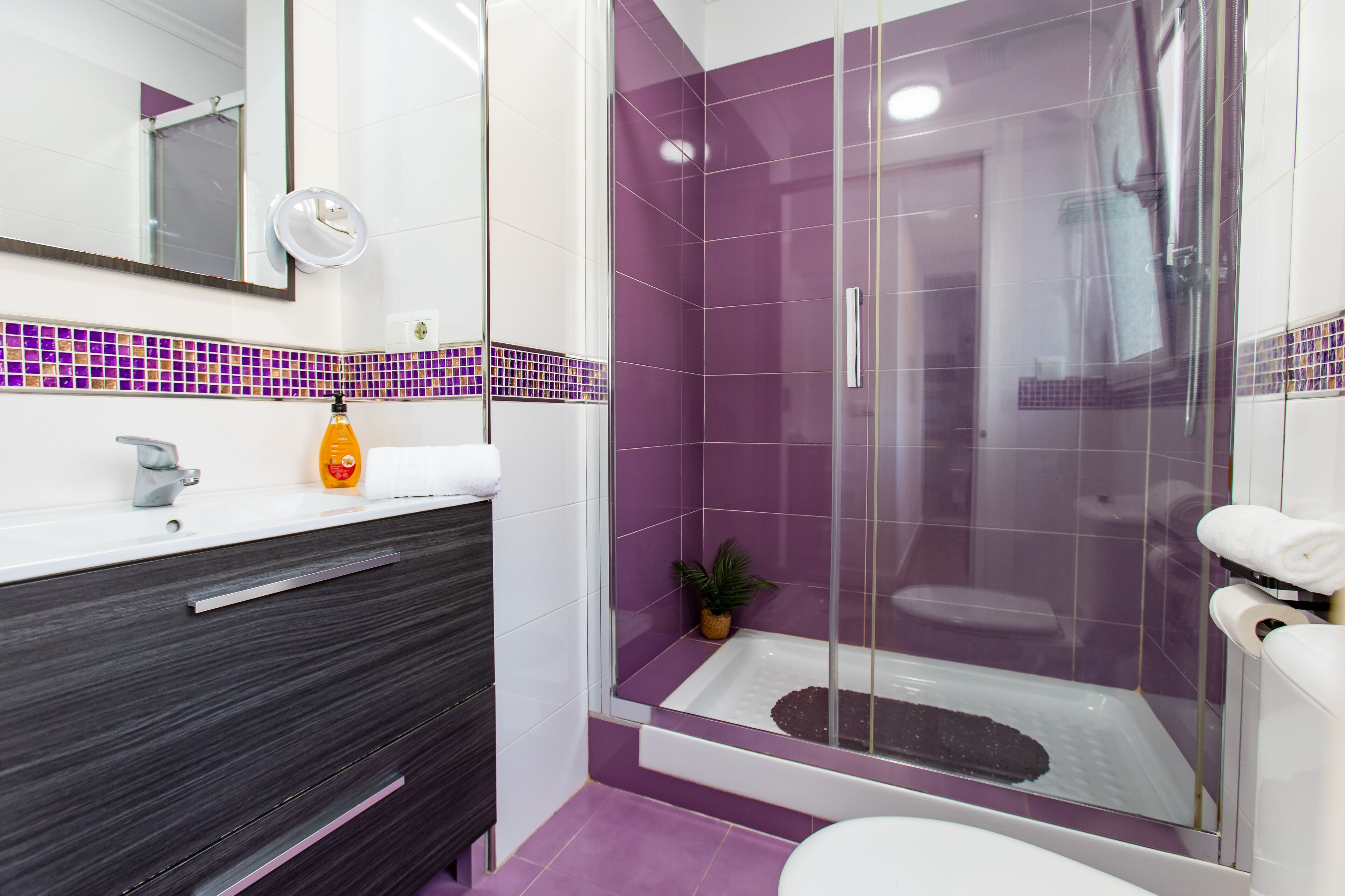 Un baño moderno con ducha envuelta en vidrio, un lavabo blanco y un mueble de tocador oscuro.