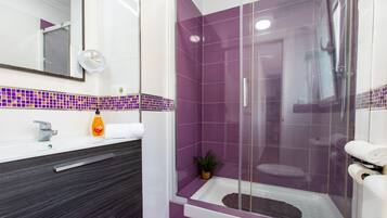 Un baño moderno con ducha envuelta en vidrio, un lavabo blanco y un mueble de tocador oscuro.