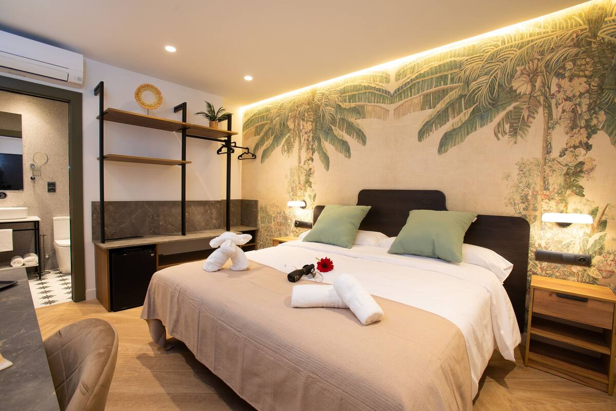 A well-lit hotel room with a large bed, a TV, a desk, and a bathroom.