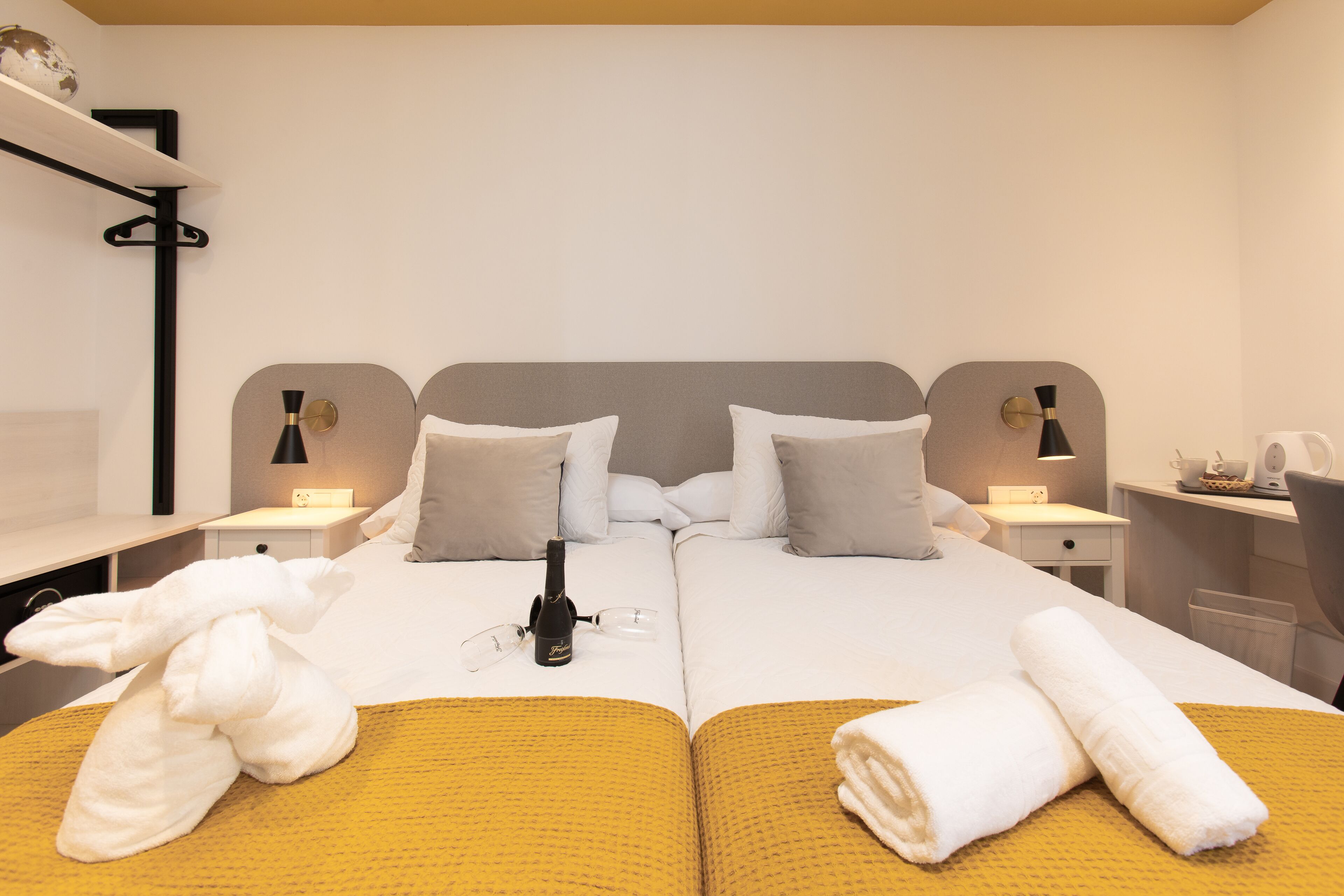Ein Doppelbett mit zwei Kissen, ein Nachttisch mit Lampe und eine Champagnerflasche.