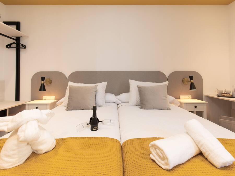 A double bed with two pillows, a bedside table with a lamp, and a bottle of champagne.