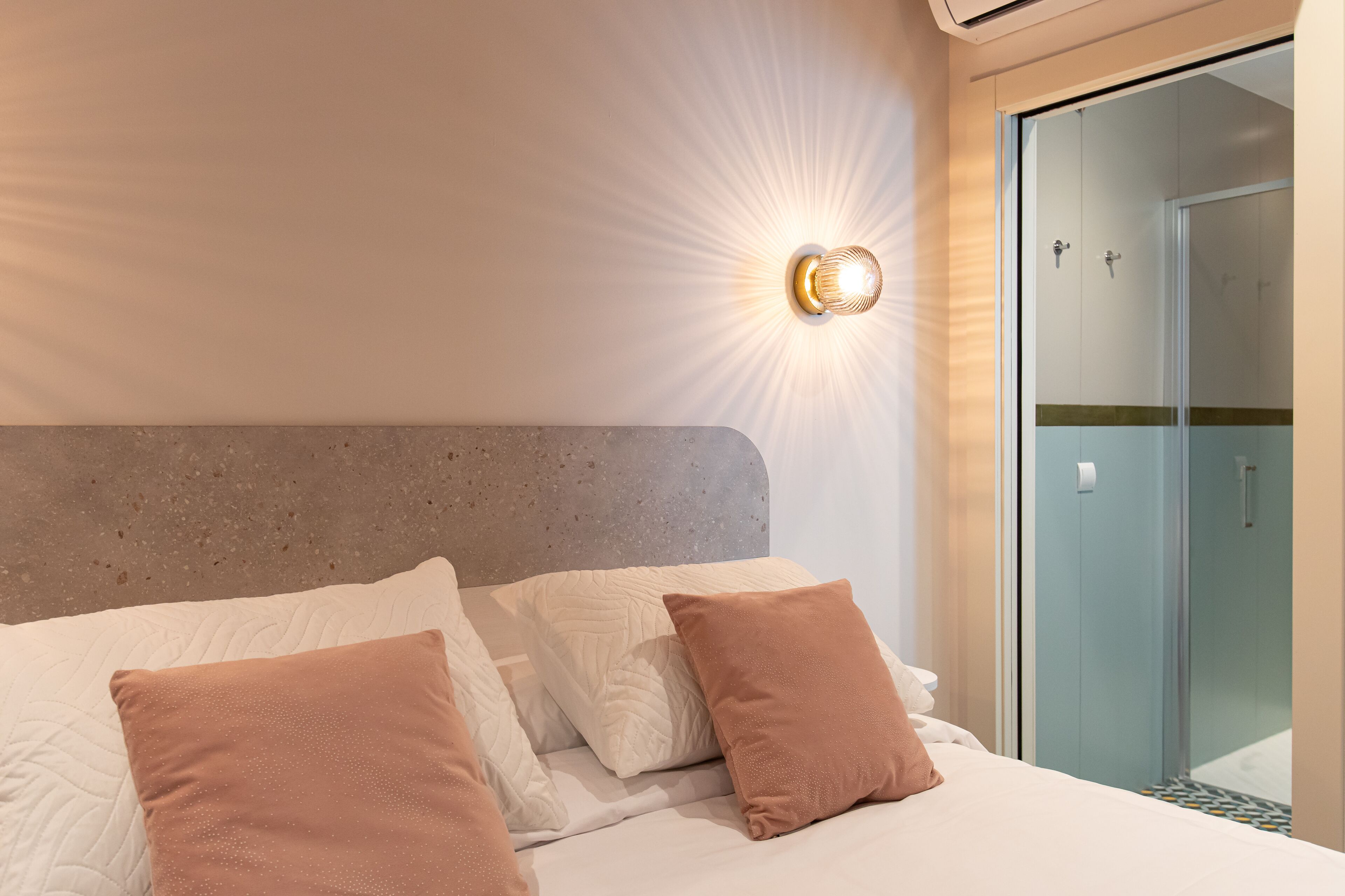 A modern hotel room with a large bed, a headboard, and a glass shower enclosure.