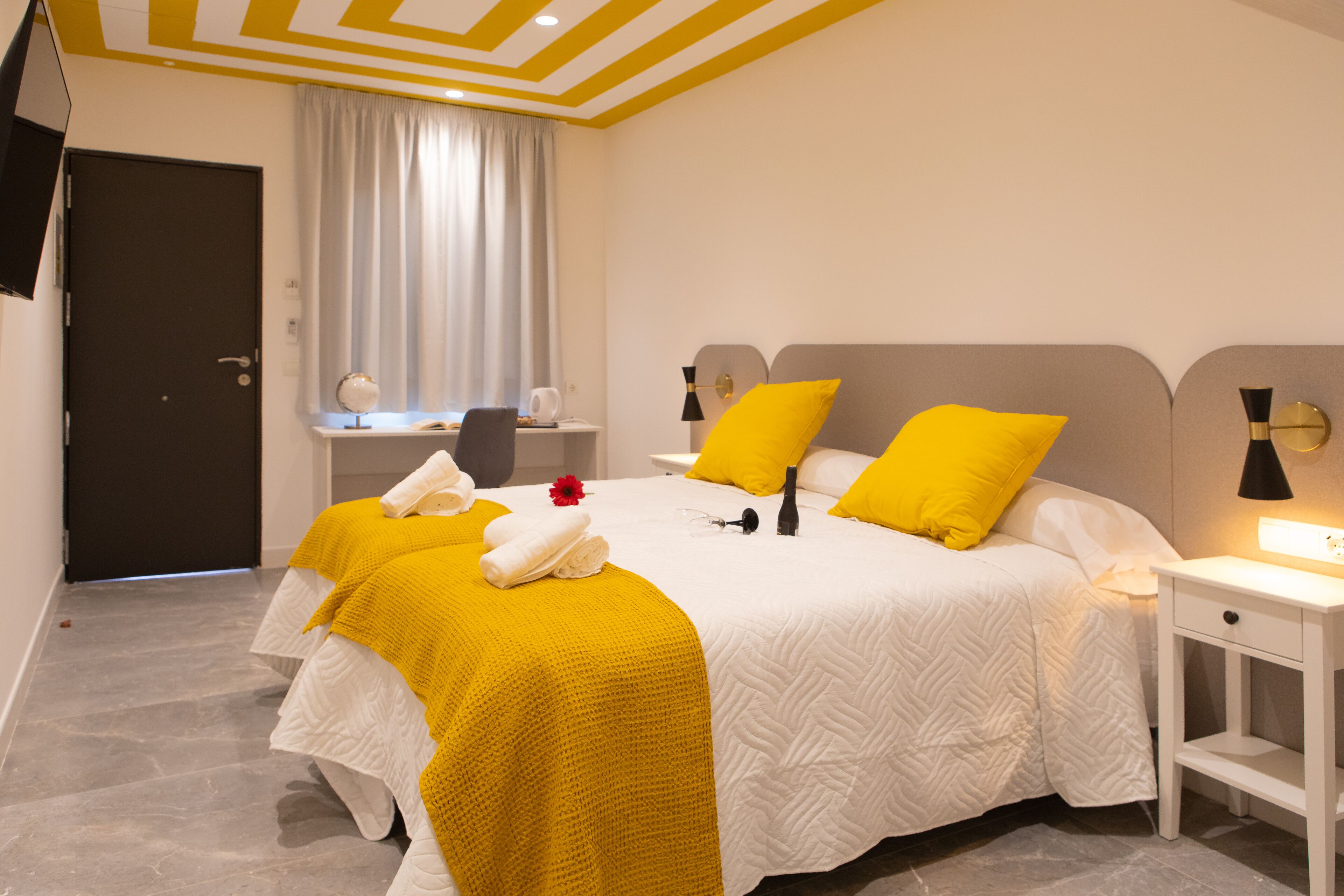 A hotel room with a large bed, a bedside table, a desk, and a chair.