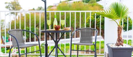 A balcony with two wicker chairs, a small round table, and a potted plant.