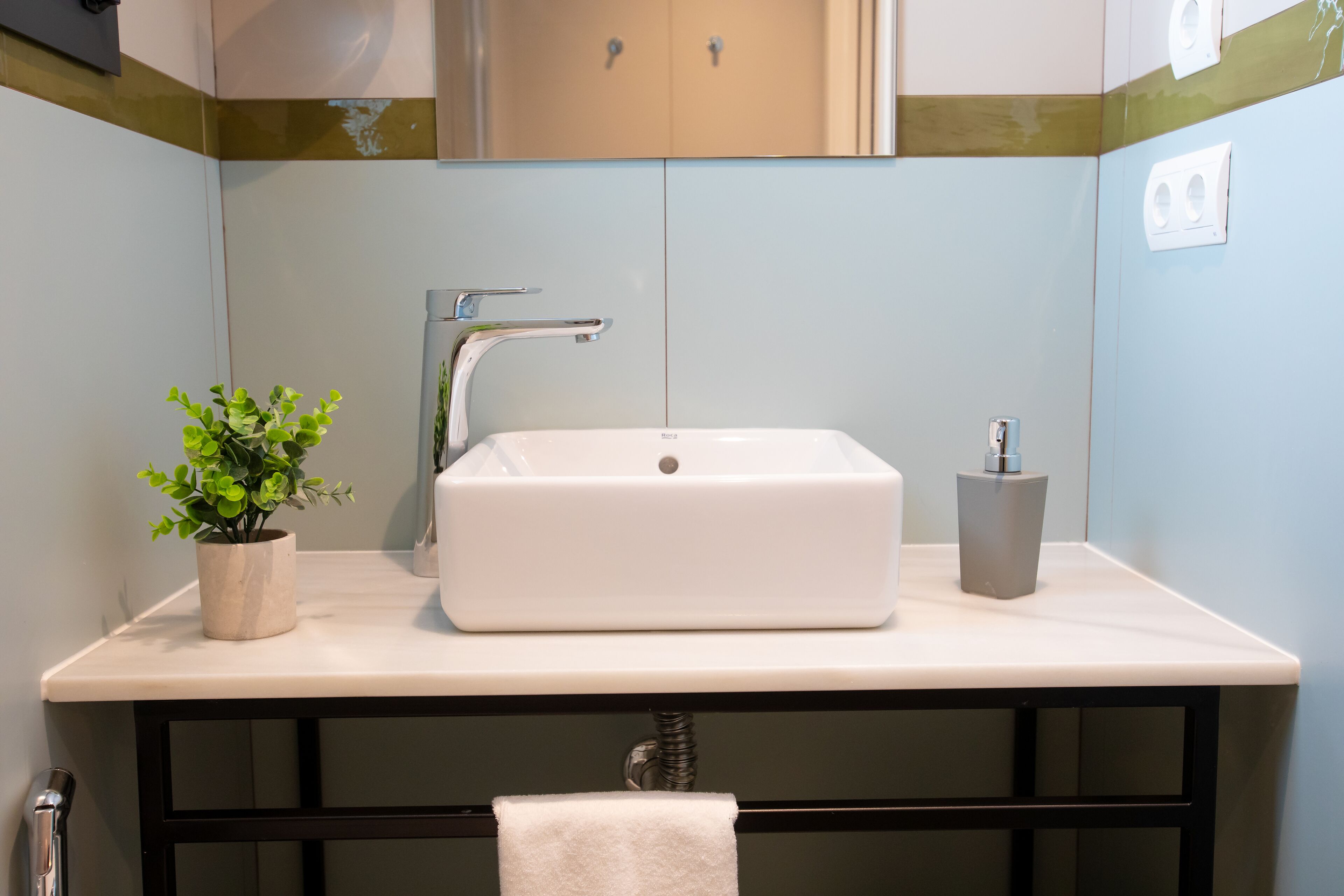 A bathroom with a white sink, a potted plant, and a towel hanging on a rack.