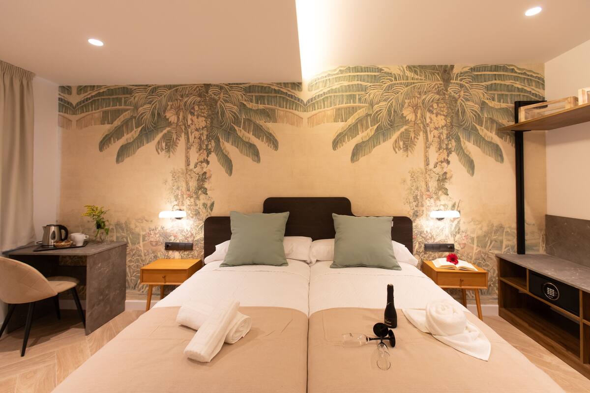 A hotel room with a large bed, two nightstands, a desk with a chair, and a wall mural.
