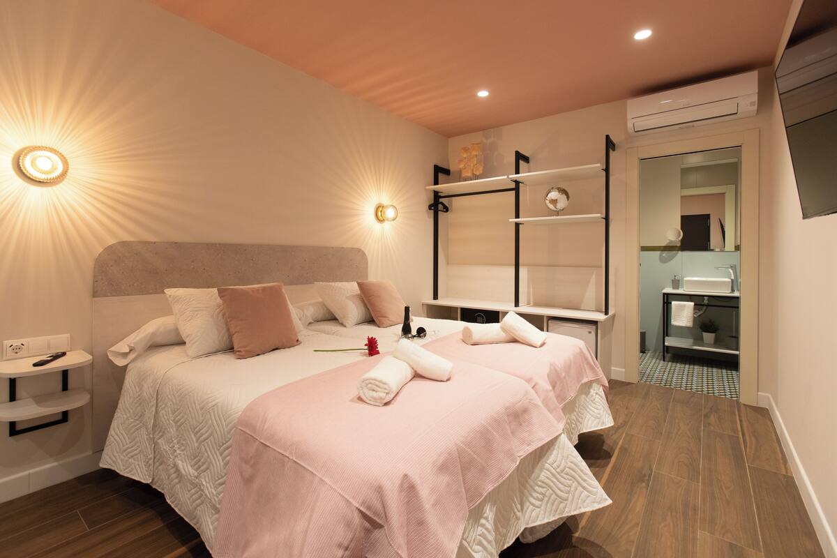 A modern hotel room with a large bed, bedside tables, a vanity with a mirror, and a shower area.