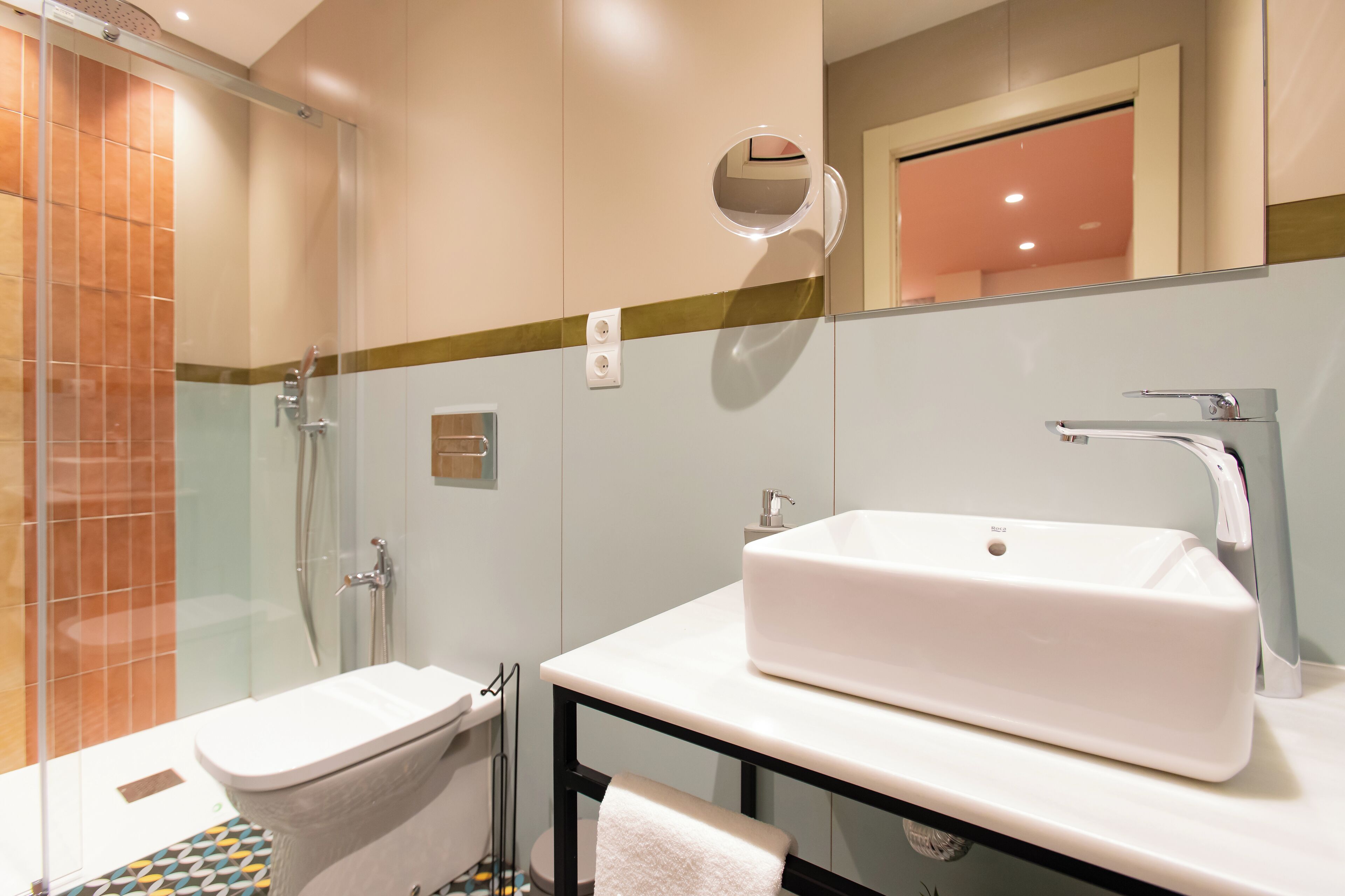 Un baño moderno con ducha envuelta en vidrio, un lavabo blanco y un espejo con marco redondo.