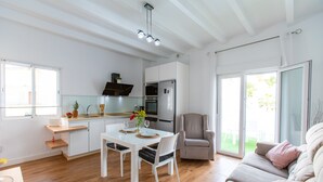 A modern kitchen with white cabinetry, a dining table with chairs, a refrigerator, and a large window.