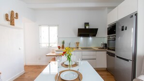 A modern kitchen with white cabinetry, a stainless steel refrigerator, and a dining area set with a white table, plates, and cutlery.