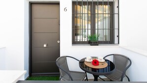 A small outdoor seating area with a table and two chairs, a dark door, and a window with metal bars.