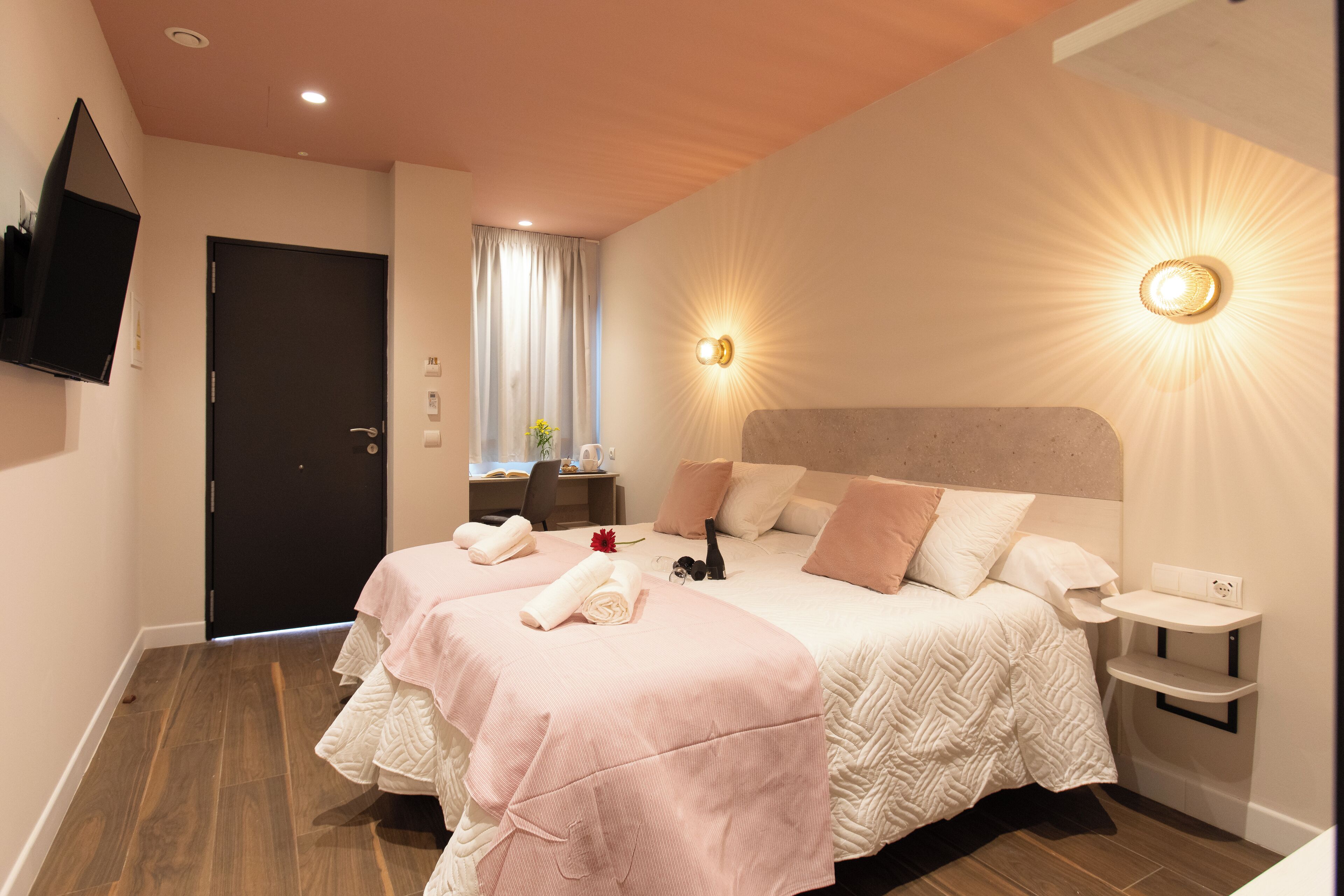A hotel room with a large bed, two bedside tables, a TV mounted on the wall, and a window with curtains.