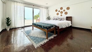Ein Schlafzimmer mit Bett, einer Bank, einer Topfpflanze, Blick auf den Strand und einer Wand mit runden Dekorationen.